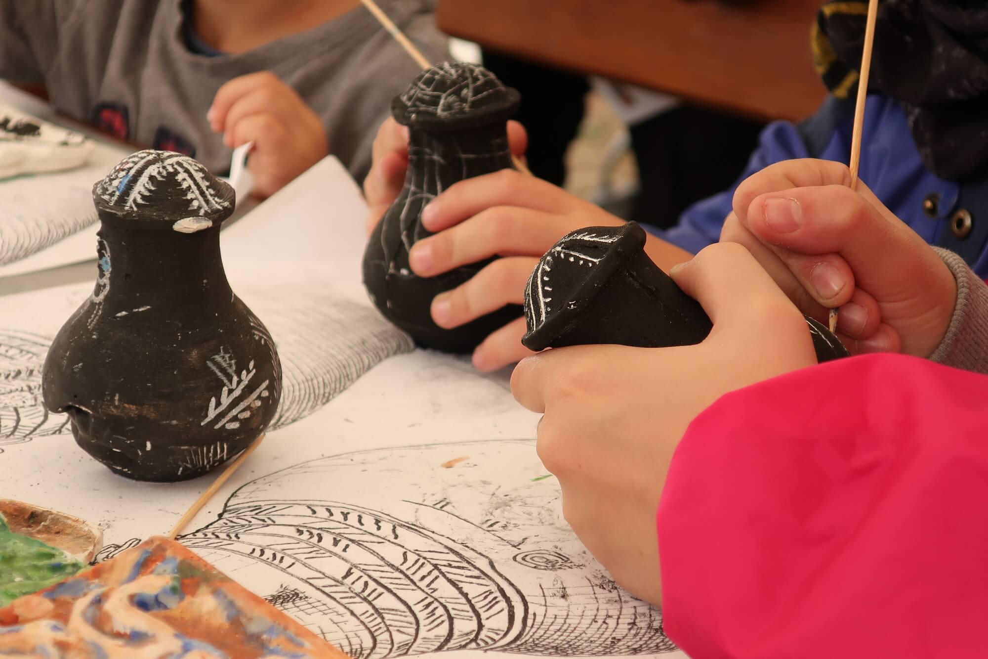 Zdjęcie przedstawia zbliżenie na dłonie dzieci, które ozdabiają małe odlewy urn twarzowych.