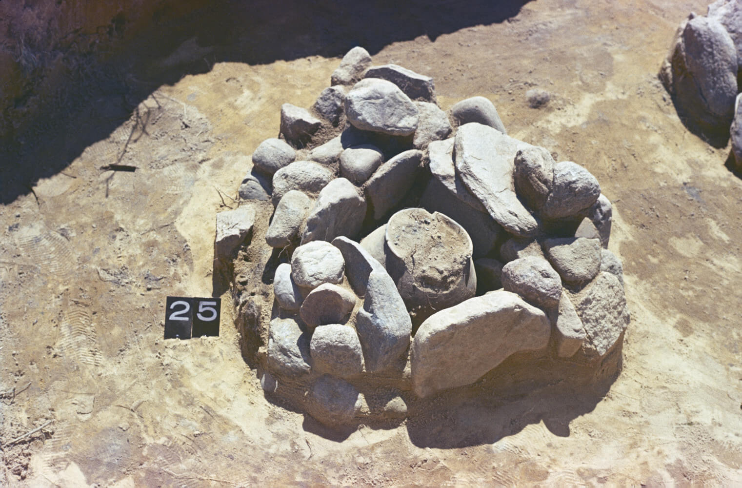 Zdjęcie z wykopalisk przedstawiające odkryty i oznaczony grób skrzynkowy, skłądający się z kamiennych płyt, które otaczają popielnicę.